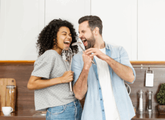 A couple singing in the kitchen with utensils.