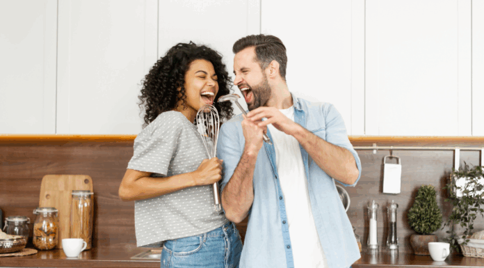 A couple singing in the kitchen with utensils.