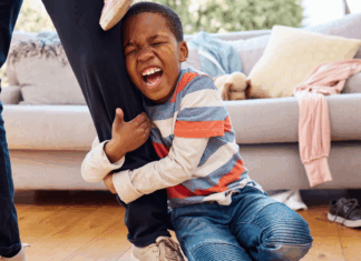 A boy having a tantrum as he holds on to an adults leg.