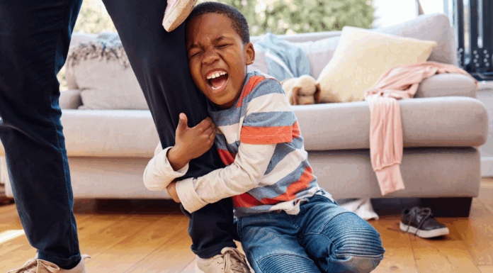 A boy having a tantrum as he holds on to an adults leg.