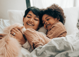 A mom laying in bed with her child and cat.