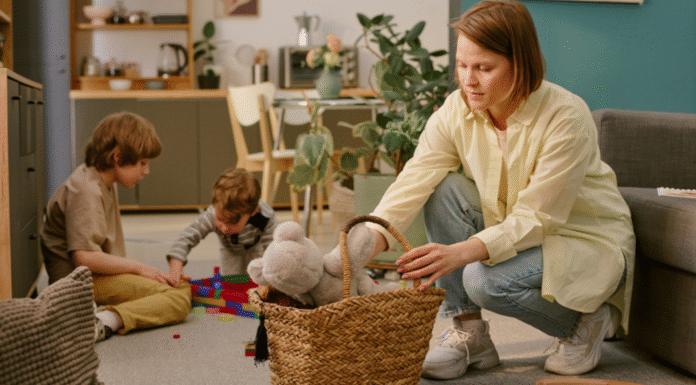 A woman picking up toys while her kids are playing.