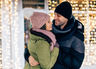 A couple embracing with holiday lights behind them.