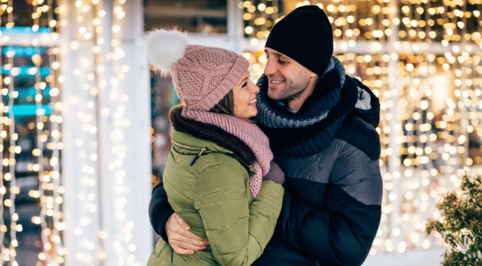 A couple embracing with holiday lights behind them.