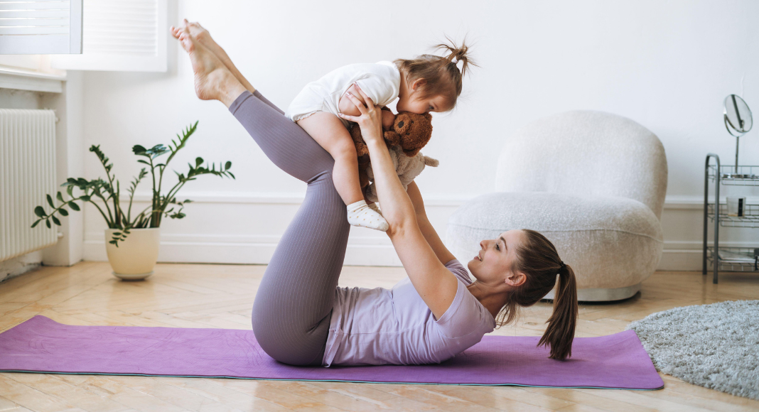 A woman doing yoga while holding her toddler.