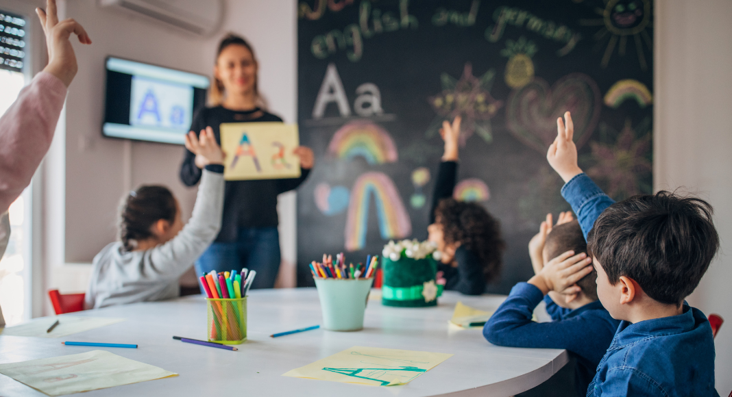 childcare and education resources A teacher standing in front of children raising their hands.
