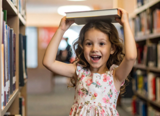 A girl in a library holding a book on her head.
