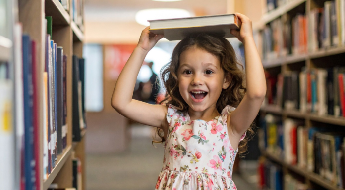A girl in a library holding a book on her head.