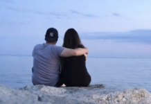 A couple sitting on the rocks at the beach watching the sunset.
