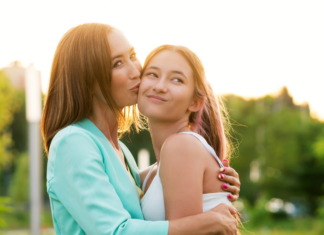 Mom kissing teen daughter on the cheek.