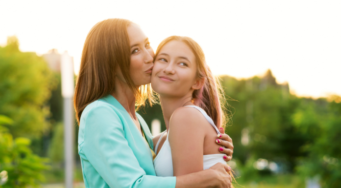 Mom kissing teen daughter on the cheek.
